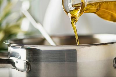 Greek extra virgin olive oil being poured into a cooking pot for Mediterranean cooking.