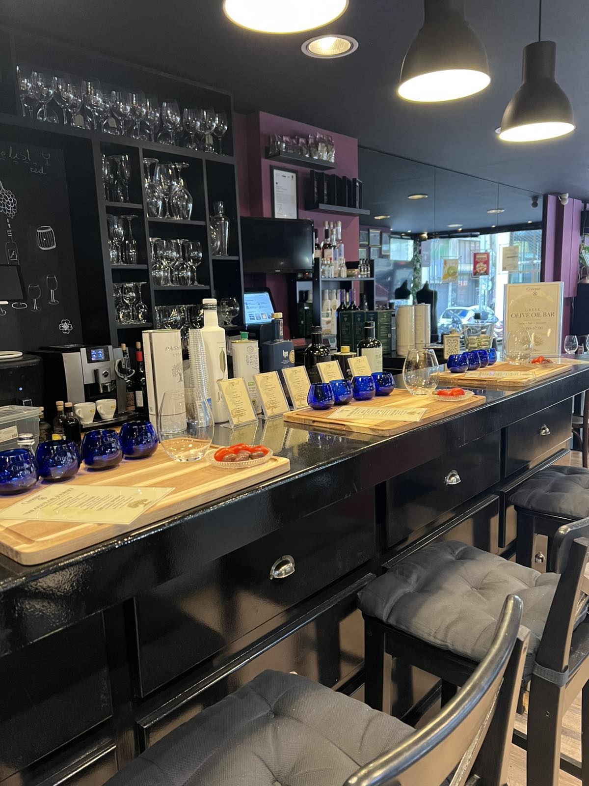 Discover the Greek Olive Oil Bar at Cinque Monastiraki The olive oil tasting counter at Cinque Monastiraki with Greek olive oils, blue tasting glasses and wooden tasting trays.